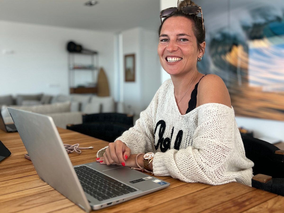 Saskia Drewicke lächelnd am Laptop an einem Holztisch